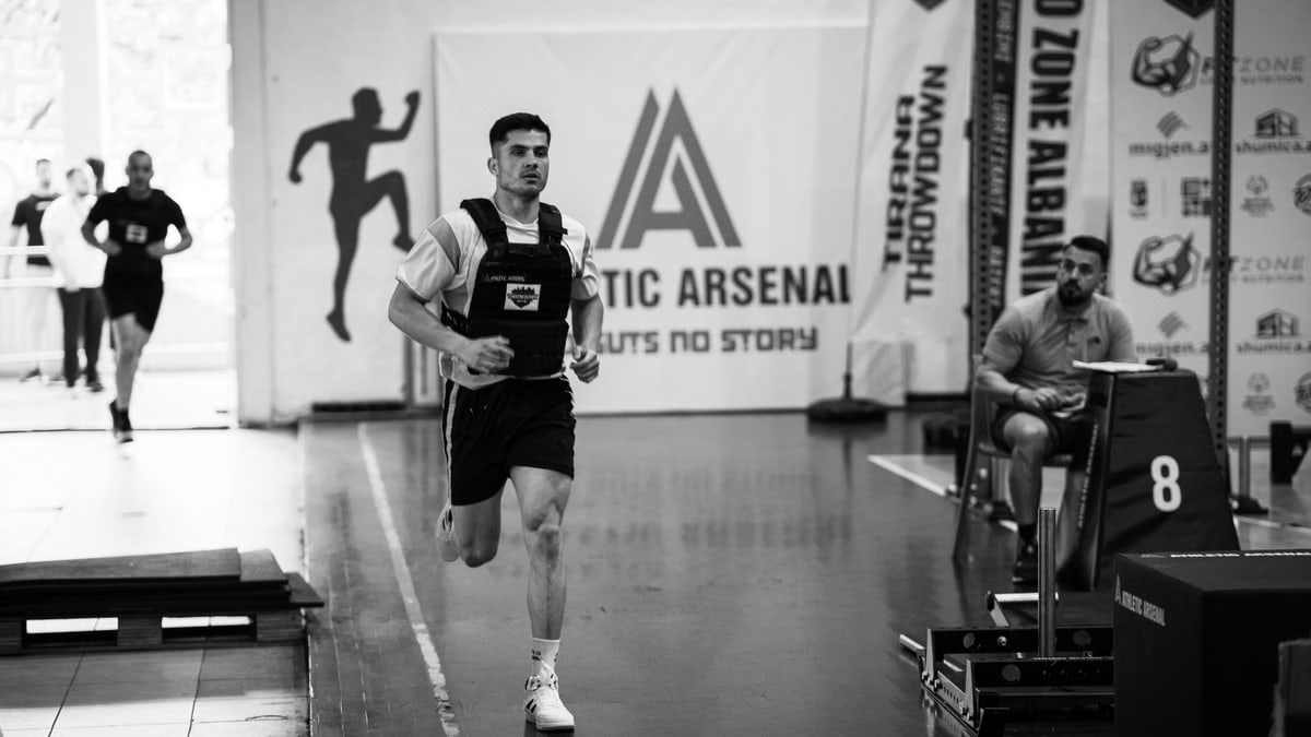 Male athlete running indoors during a competitive sports event with fitness branding.